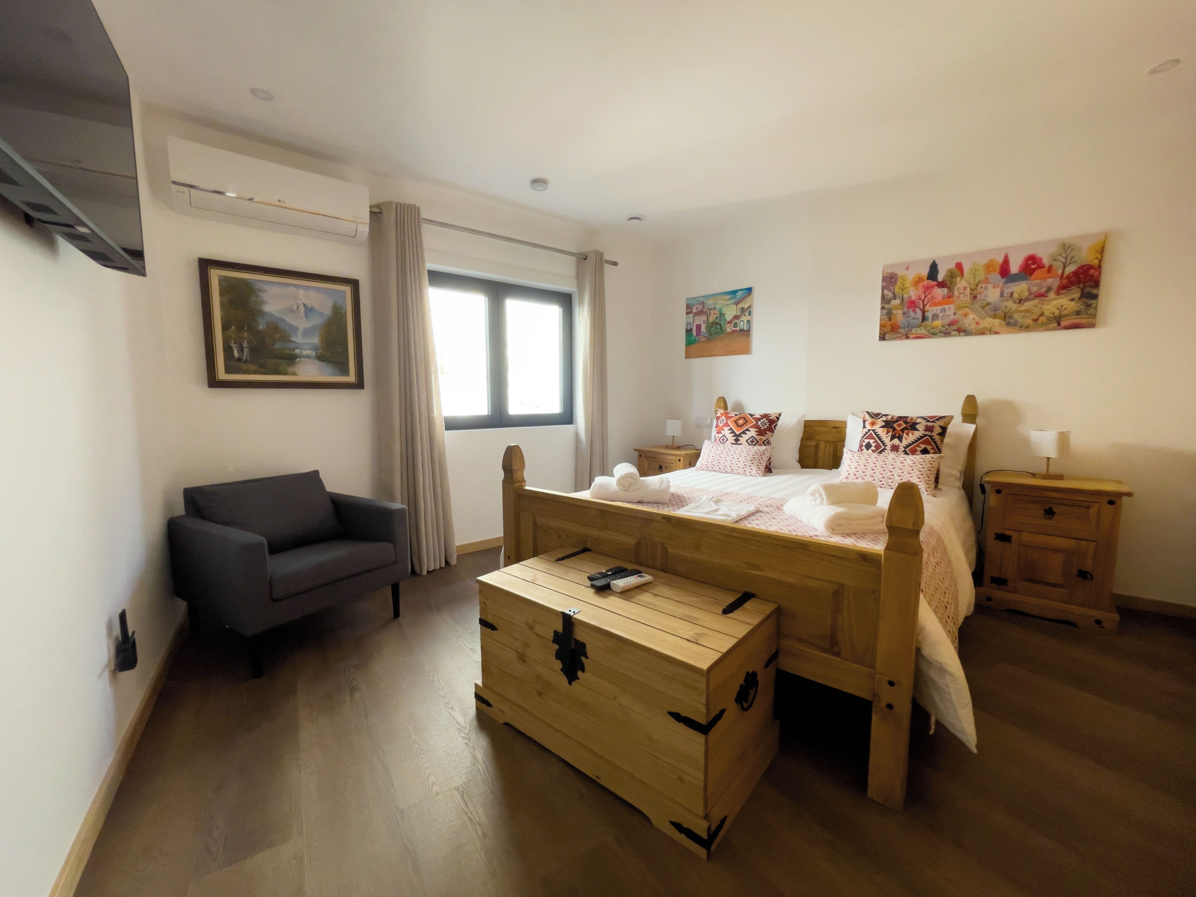 Quarto com cama, um baú de madeira, sofá, mesa de cabeceira e um quadro na parede.