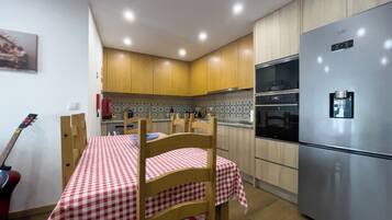 A kitchen with wooden cabinets, a stainless steel refrigerator, a checkered tablecloth, and a guitar leaning against the wall.