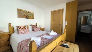 A hotel room with a bed, bedside tables, a painting, a wardrobe, and a bathroom visible through an open door.