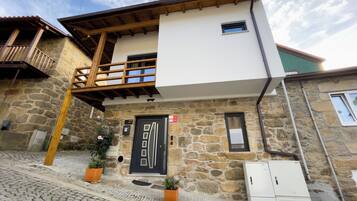 A two-story building with a stone facade, a wooden balcony, and a black door with a number plaque.