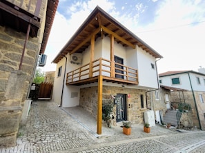 Un edificio de dos pisos con fachada de piedra, balcón de madera y una calle adoquinada.