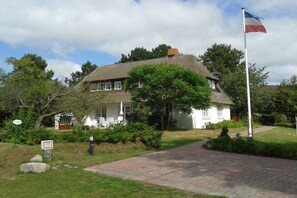 Et traditionelt hus med stråtækt tag, et flagstang med flag og en belagt indkørsel.