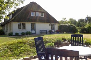 Ein Haus mit einem Reetdach, einer weißen Fassade und einer Veranda mit einer Bank.