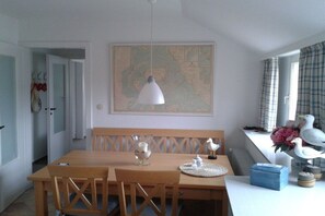 Ein Essbereich mit Holztisch und Stühlen, einer Karte an der Wand und Dekorationselementen, darunter eine Vogelstatue und eine Vase mit Blumen.