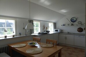 Et køkken med spisebord, stole, en hængende lampe og et vindue med gardiner.