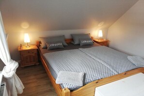 A single-bed room with a wooden frame, two bedside tables with lamps, and two pillows with text. - Holiday apartment in Föhr with 1 bedroom (Nieblum)