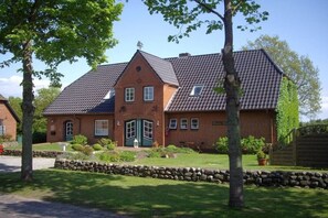 A two-story house with a stone foundation, a tiled roof, and a front entrance with a green door. - Holiday apartment in Föhr with 1 bedroom (Nieblum)
