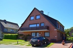 Ein zweistöckiges Backsteinhhaus mit Balkon, einem parkenden Auto und einem gepflegten Rasen.
