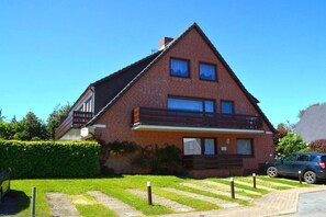 A two-story brick house with a balcony, a car parked in the driveway, and a well-maintained lawn. - Holiday apartment in Föhr with 1 bedroom (Wyk auf Föhr)