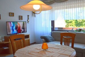 Ein Wohnzimmer mit Fernseher, einem Tisch mit Kerze und einer Couch.