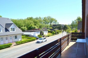 A residential street with a white car parked on the side, a white house with a grey roof, and a green hedge. - Holiday apartment in Föhr with 1 bedroom (Wyk auf Föhr)