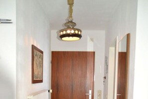A hallway with a wooden door, a framed picture on the wall, a ceiling light fixture, and a radiator. - Holiday apartment in Föhr with 1 bedroom (Wyk auf Föhr)