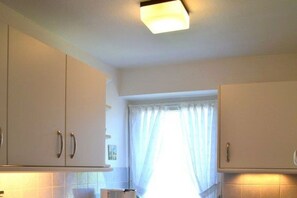 Eine Küche mit weißen Schränken, einer Deckenleuchte und einem Fenster mit Vorhängen.