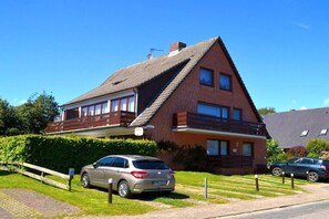A two-story house with a sloped roof, a balcony on the upper floor, and a car parked in the driveway. - Holiday apartment in Föhr with 1 bedroom (Wyk auf Föhr)