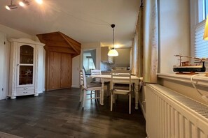 A dining area with a table and chairs, a white cabinet with glass doors, and a wooden ceiling structure. - Holiday apartment in Föhr with 1 bedroom (Nieblum)