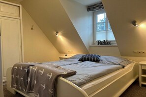 A bedroom with a bed, a nightstand, a window with a view, and a wall-mounted light fixture. - Holiday apartment in Föhr with 1 bedroom (Nieblum)
