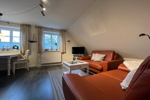 A cozy living room with a sofa, a television, and a dining area with a table and chairs. - Holiday apartment in Föhr with 1 bedroom (Nieblum)