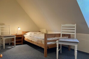 A small, cozy room with a sloped ceiling, a single bed, two chairs, a nightstand with a lamp, and a carpeted floor. - Holiday apartment in Föhr with 1 bedroom (Nieblum)