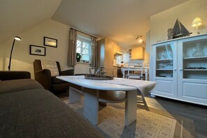 A cozy living room with a sofa, a dining table, and a cabinet with glassware. - Holiday apartment in Föhr with 1 bedroom (Nieblum)