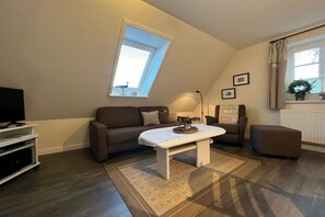 Sala de estar com sofá, mesa de centro, TV e janela com cortinas.