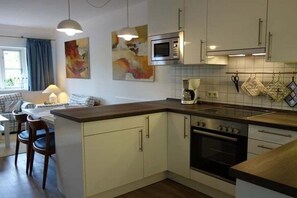 A modern kitchen with white cabinets, a built-in oven, and a microwave. There is a dining area with a table and chairs. - Holiday apartment in Föhr with 1 bedroom (Wrixum)
