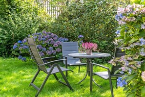 A garden with a round table and two chairs, surrounded by lush greenery and purple flowers. - Reethus WE 3, Blue mussel (Borgsum)