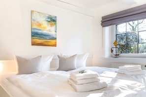 A hotel room with a bed, pillows, a painting, a window with curtains, and a radiator. - Reethus WE 3, Blue mussel (Borgsum)