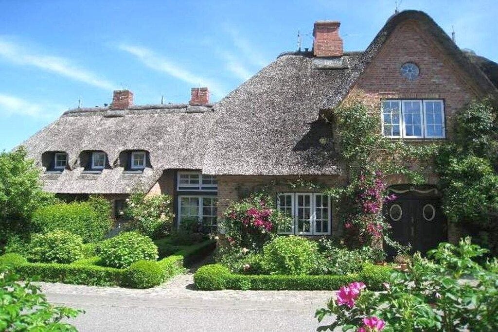 A traditional thatched-roof house with a brick chimney, a window with a white frame, and a door with a circular design.