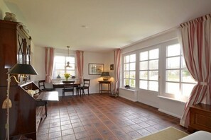 A dining area with a table and chairs, a lamp, and a window with curtains. - Holiday apartment in Föhr with 1 bedroom (Nieblum)