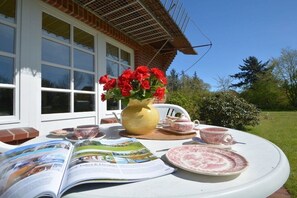 Una mesa dispuesta con un florero de flores rojas, una tetera, tazas y platillos, y una revista.