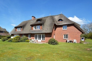 A large brick house with a thatched roof, a well-maintained lawn, and a patio area with outdoor furniture. - Holiday apartment in Föhr with 1 bedroom (Nieblum)