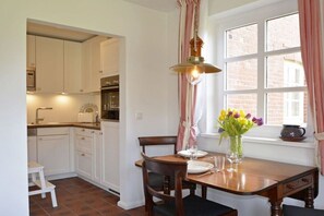 A dining area with a wooden table, chairs, and a vase of flowers. - Holiday apartment in Föhr with 1 bedroom (Nieblum)