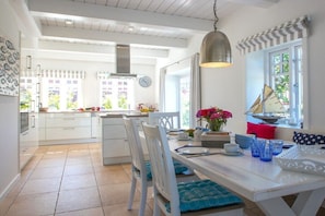 A bright kitchen with white cabinets, a dining table set with blue glassware, and a hanging light fixture. - Holiday home in Oldsum with swimming pool (Oldsum)