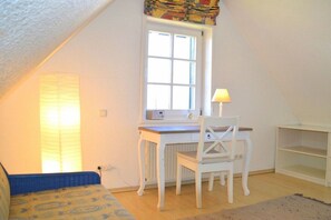 A room with a sloped ceiling, a desk with a chair, a window with blinds, and a bed with a patterned bedspread. - Holiday home in Oldsum with swimming pool (Oldsum)