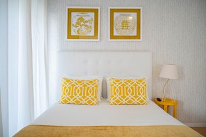 Habitación de hotel con una cama, dos almohadas, una mesita de noche, una lámpara y dos cuadros en la pared.