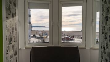 Een kamer met uitzicht op een strand en een parkeerplaats, zichtbaar door twee ramen.