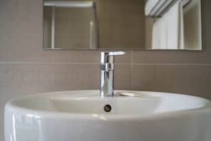 Un bany amb un lavabo blanc, aixeta cromada i un mirall a sobre.