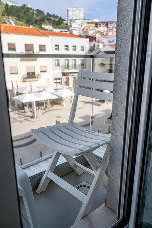 A white chair on a balcony with a view of buildings and a clear sky.