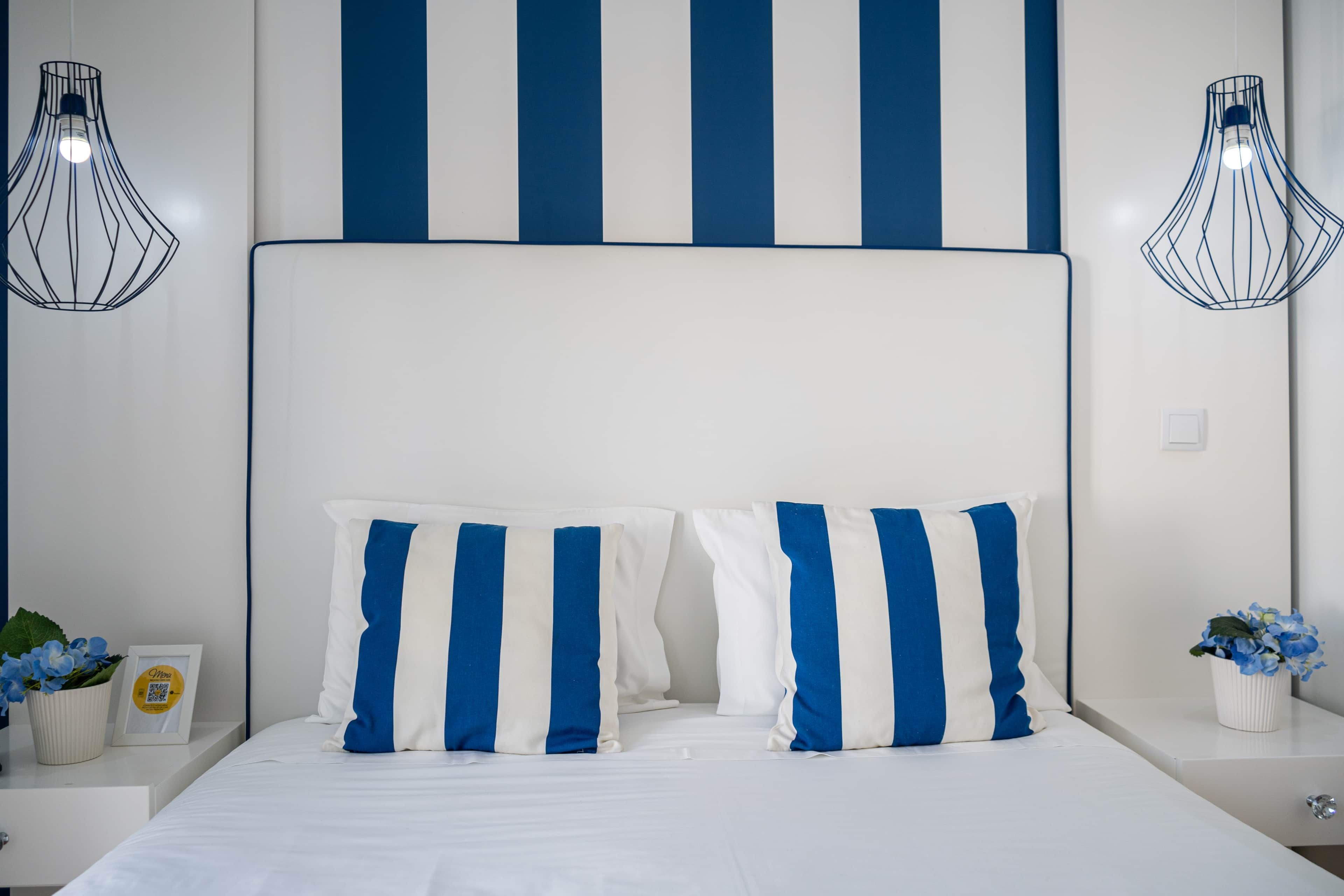 Ein Bett mit weiß-blauen Kissenstreifen, einem weißen Kopfteil und zwei Wandleuchten.