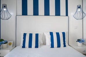 A bed with white and blue striped pillows, a white headboard, and two wall-mounted lamps. - Double Room Square and Sea View (Nazaré)