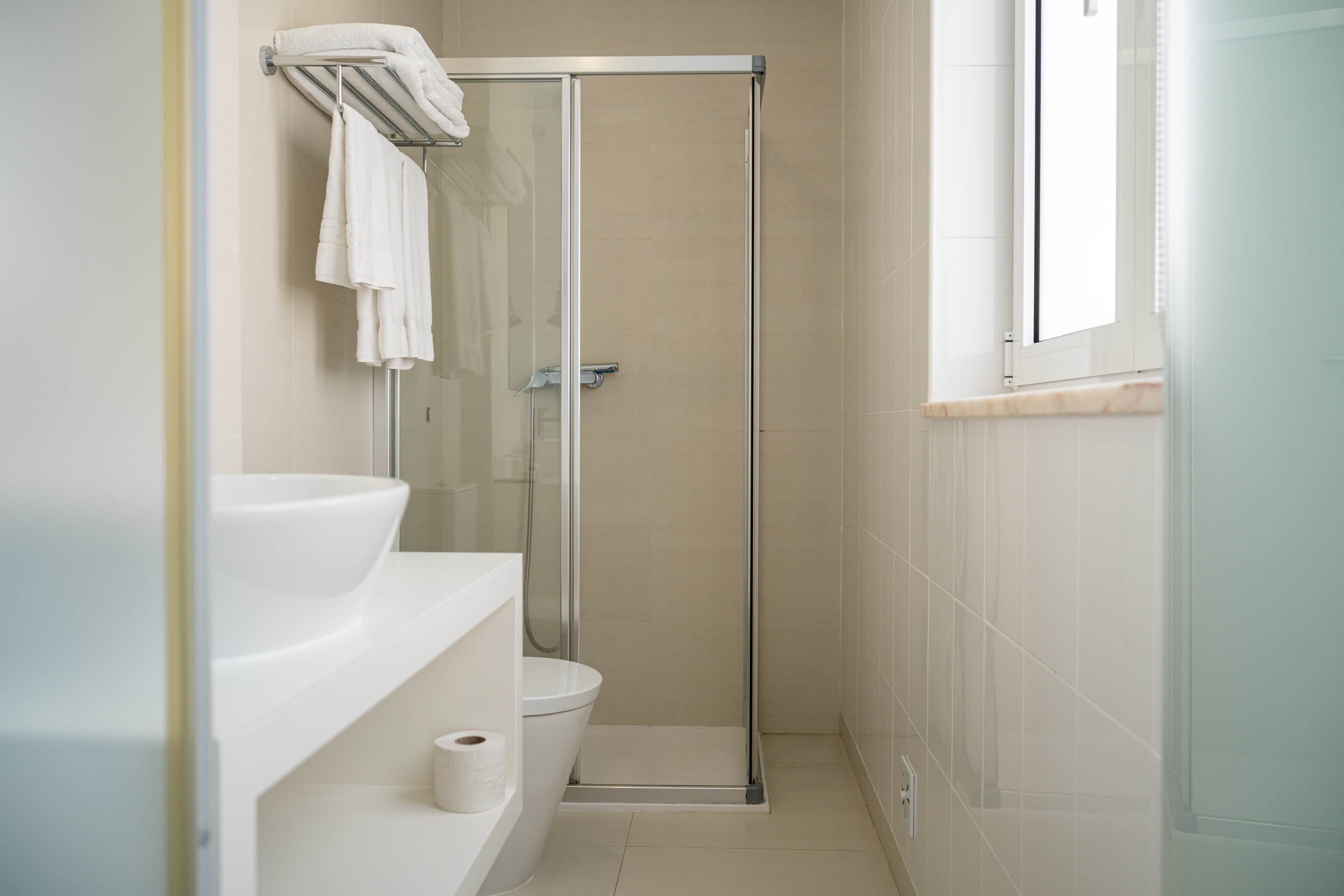 A modern bathroom with a glass shower enclosure, a toilet, and a sink with a towel rack above it.