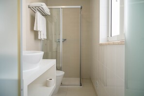 Un baño moderno con cabina de ducha de vidrio, inodoro y lavamanos con toallero arriba.