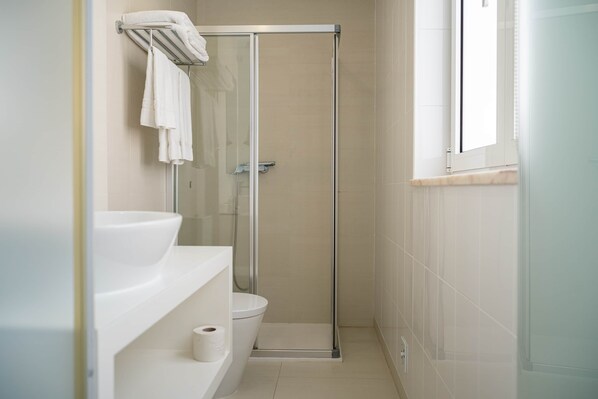 Une salle de bain moderne avec une douche à parois de verre, des toilettes et un lavabo surmonté d’un porte-serviettes.