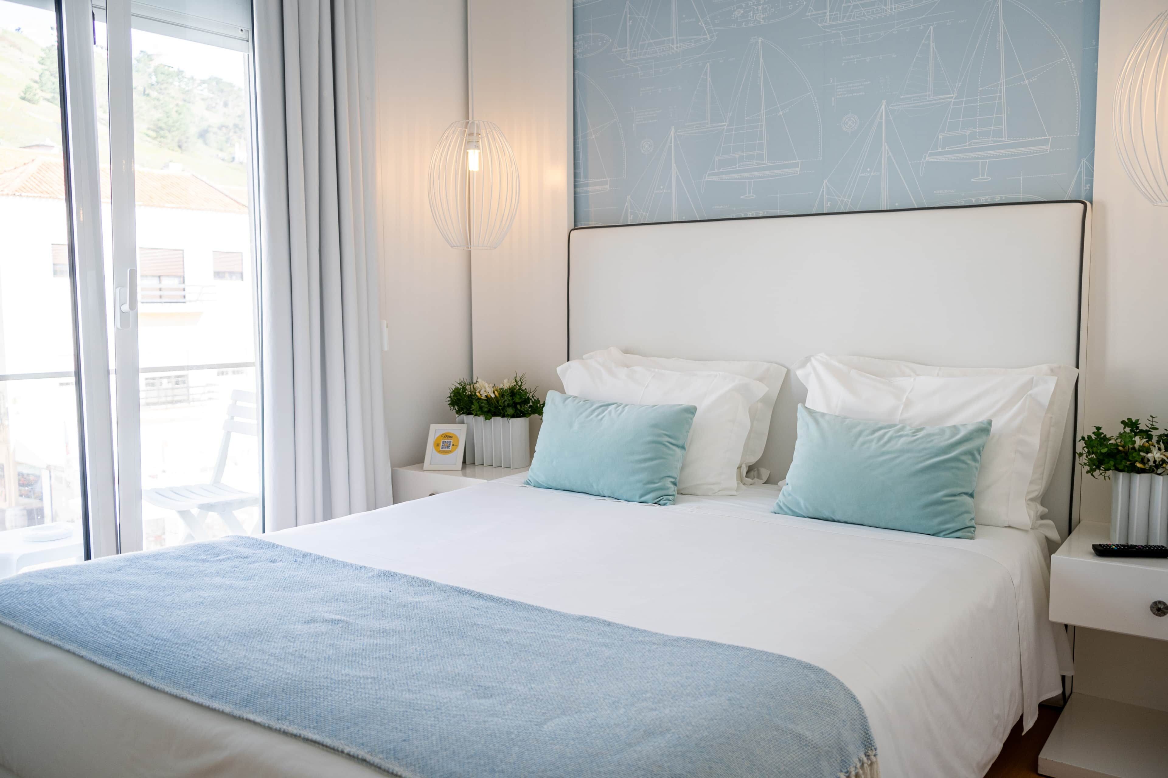 Een slaapkamer met een groot bed, een nachtkastje, een wandlamp en een raam met gordijnen.