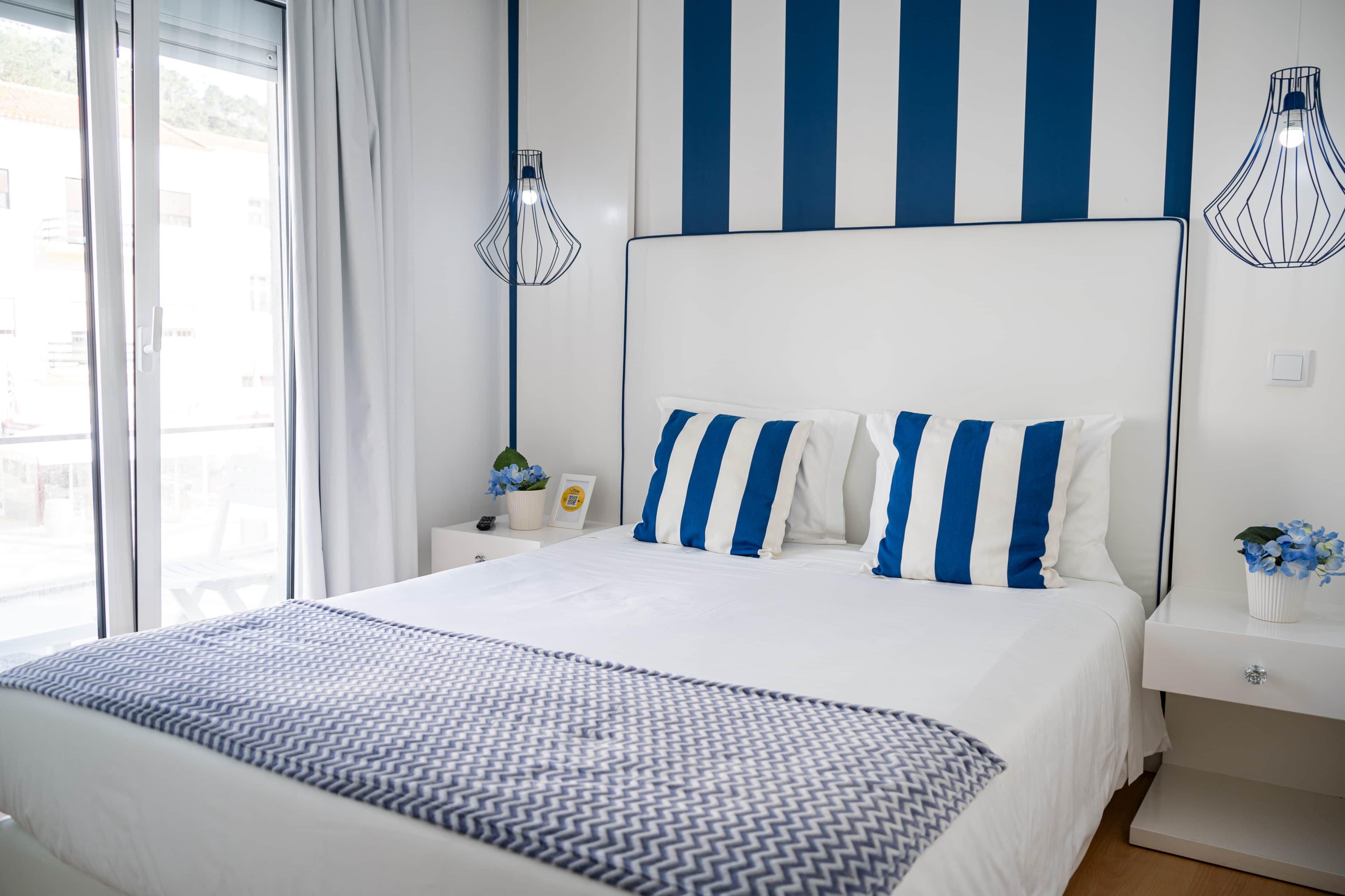 Ein Hotelzimmer mit einem großen Bett, einem Nachttisch, einer Wandlampe und Blick durch ein Fenster.