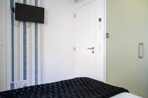 Una habitación con una cama, un televisor montado en la pared y una puerta con manija.
