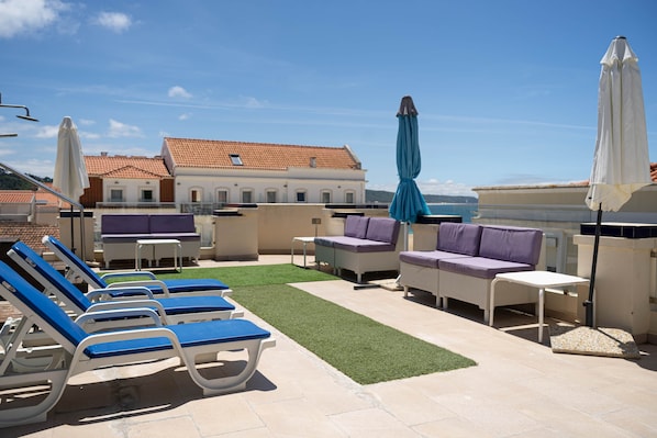 A rooftop terrace with lounge chairs, a small table, and umbrellas.