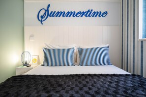 A bed with striped pillows, a white headboard, and a wall sign reading 'Summertime'. - Double Room Street View (Nazaré)