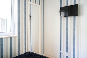 Una habitación con una puerta, televisor montado y una ventana.