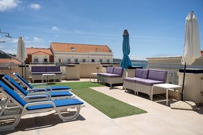 A rooftop terrace with lounge chairs, a small table, and umbrellas.